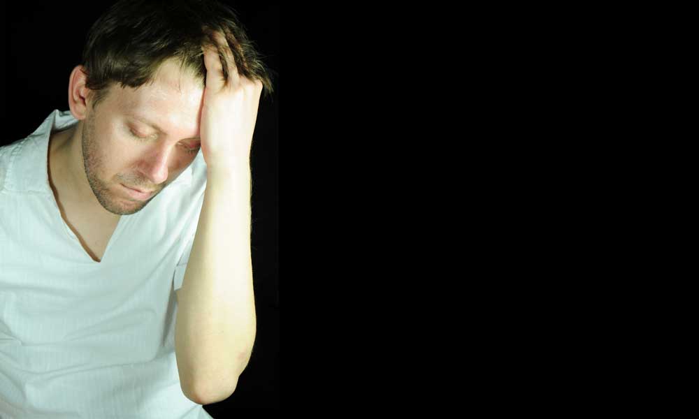 Andropause symptoms — man holding head and looking down on black background