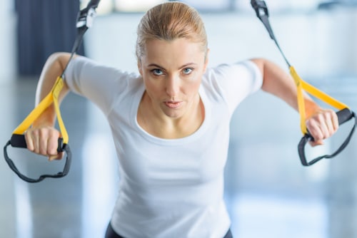 Una mujer se ejercita en una máquina con una mirada de intenso esfuerzo. Los mejores ejercicios para el desequilibrio hormonal son los mismos para hombres y mujeres. Más información.