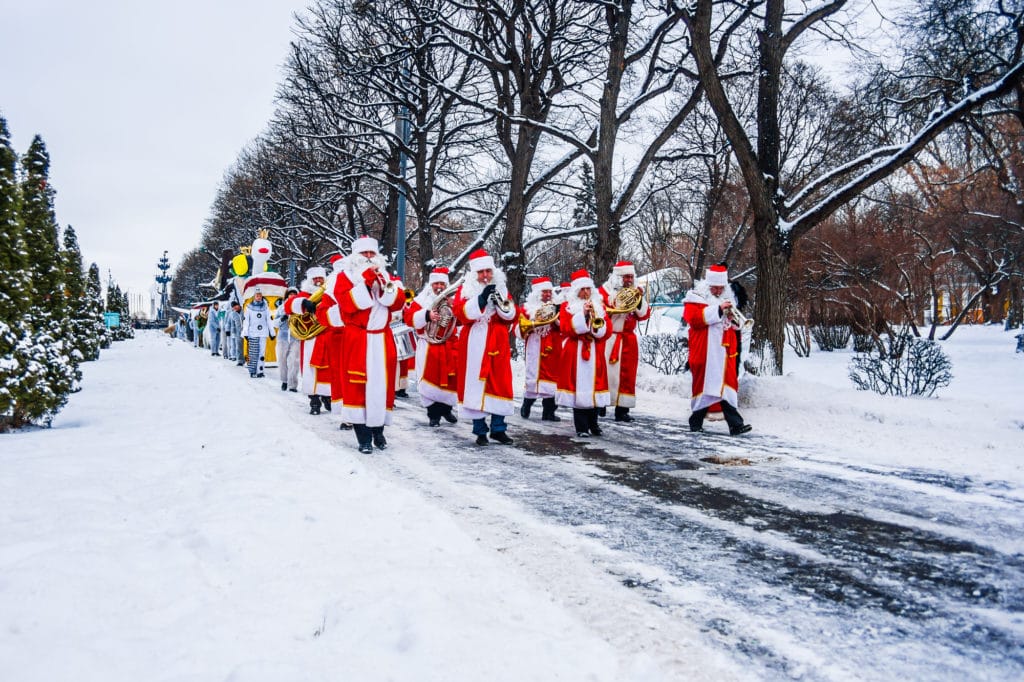 Un desfile de Papás Noel tocando instrumentos musicales marcha por un parque cubierto de nieve. El desfile de Navidad es uno de los eventos festivos anuales que se celebran en Frisco.