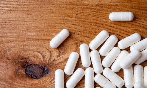 Píldoras blancas sobre una mesa de madera que podrían parecerse a la testosterona sublingual. Generalmente no se recomienda la testosterona sublingual. He aquí por qué.