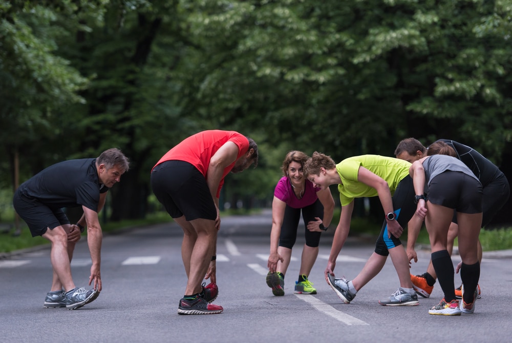 A circle of local runners stretch their hamstrings on a park road, possibly one of the free Lewisville meetups available.