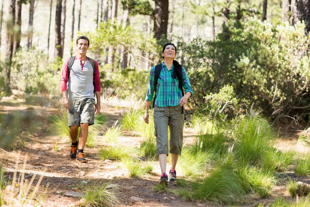 A man and women carrying backpacks are hiking near Lake Lewisville.
