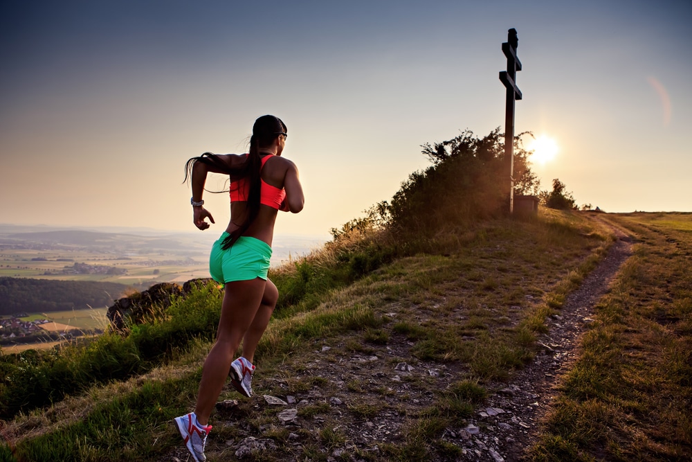 A young woman in athletic attire runs up a mountain trail. Lewisville running events provide opportunities for fun and fitness.