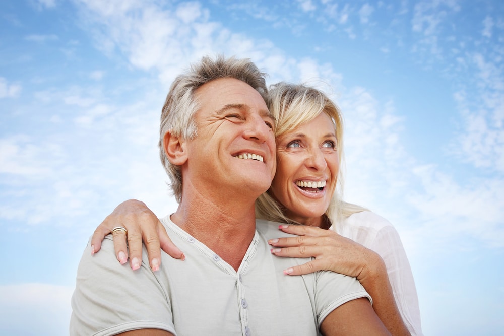 A happy couple is pictured against a blue sky. They are smiling, and the woman may be feeling better as a result of treatment for low estrogen in women.