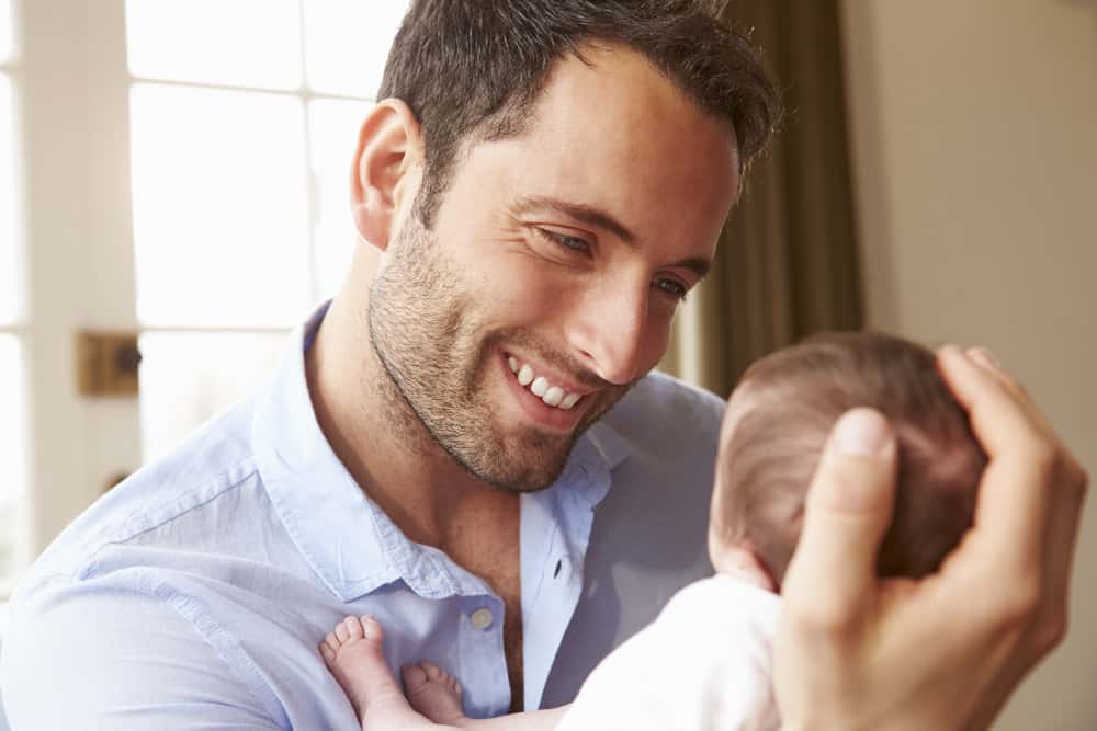 A man smiles while holding a newborn baby. Many men have questions about TRT and fertility.