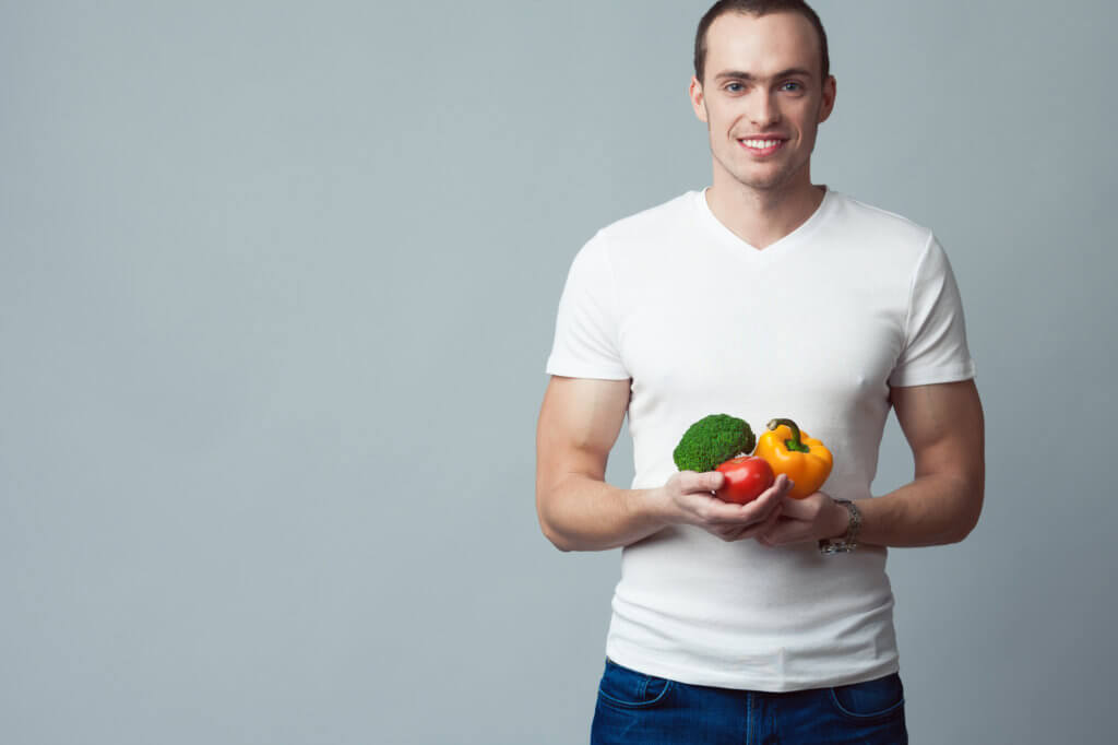 Young man in a white t-shirt holds fresh vegetables. Medical research shows that a low-fat diet can contribute to low testosterone under some circumstances.