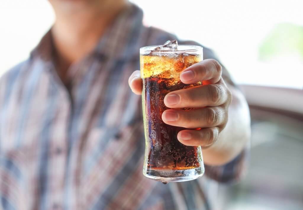 A man is holding out a sugary cola. Drinking too many sugar filled beverages could contribute to low testosterone.