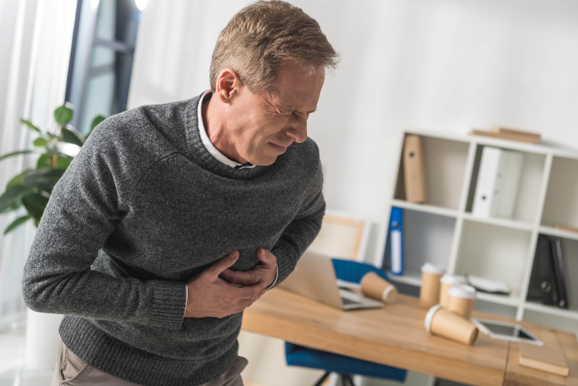 A man in a gray sweater clutches his chest, apparently from a heart attack. Research shows TRT is likely not the cause.