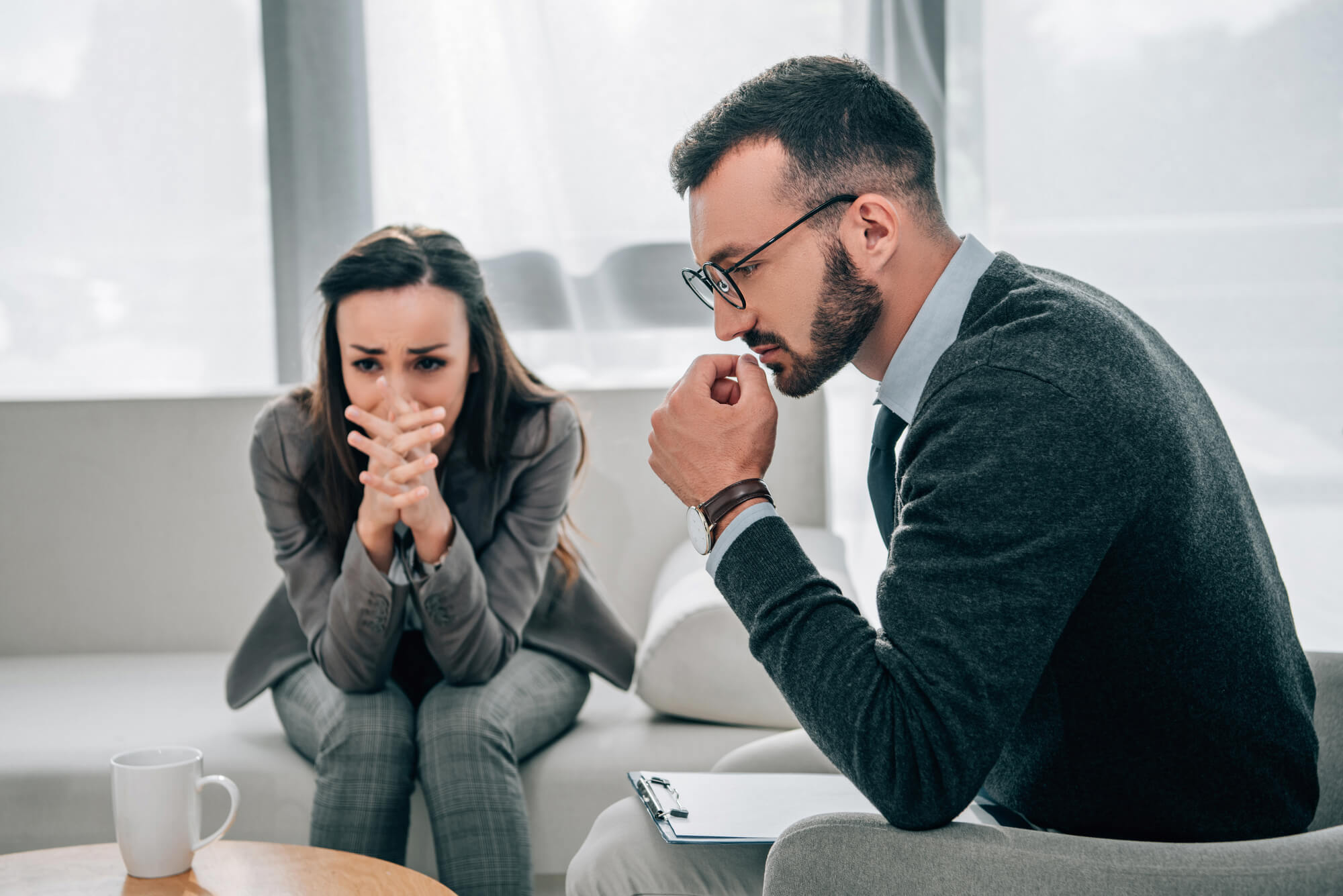 A man in a green sweater and tie sits in a doctors office with his wife, who is visibly sad. They may be asking, "Is Low T Dangerous?"