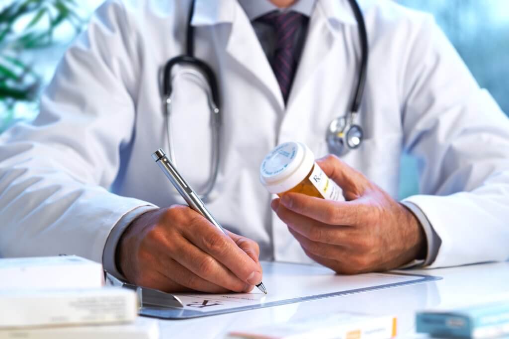 A doctor with a stethoscope around his neck writes a prescription, possibly unaware of the connection between opiates and low testosterone.