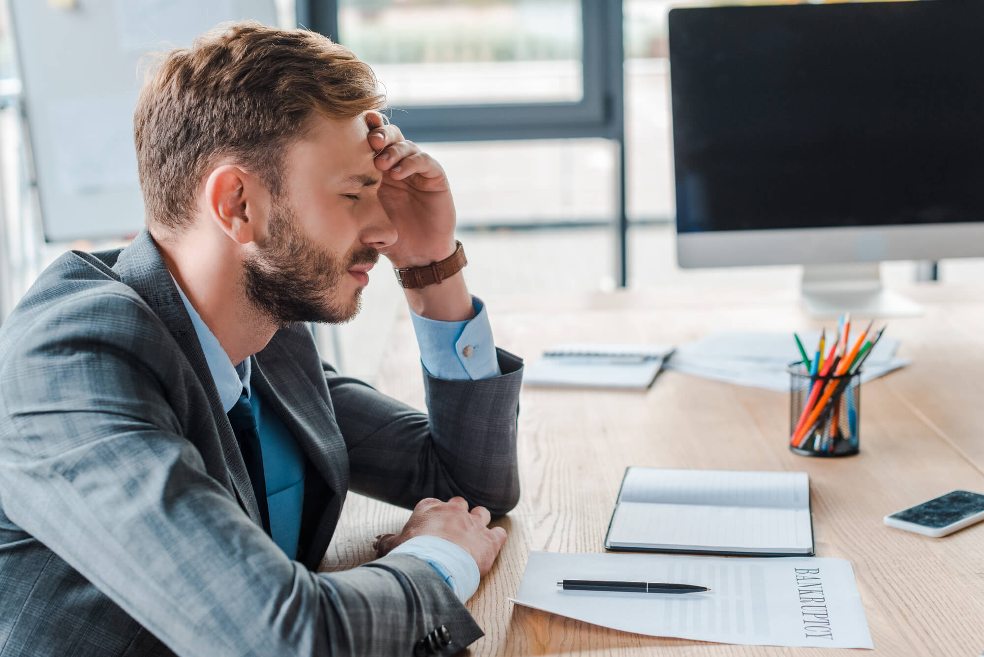 A man in a gray suit sits at a desk with his head resting on his hand. He may be worried about the connection between low testosterone and dementia..