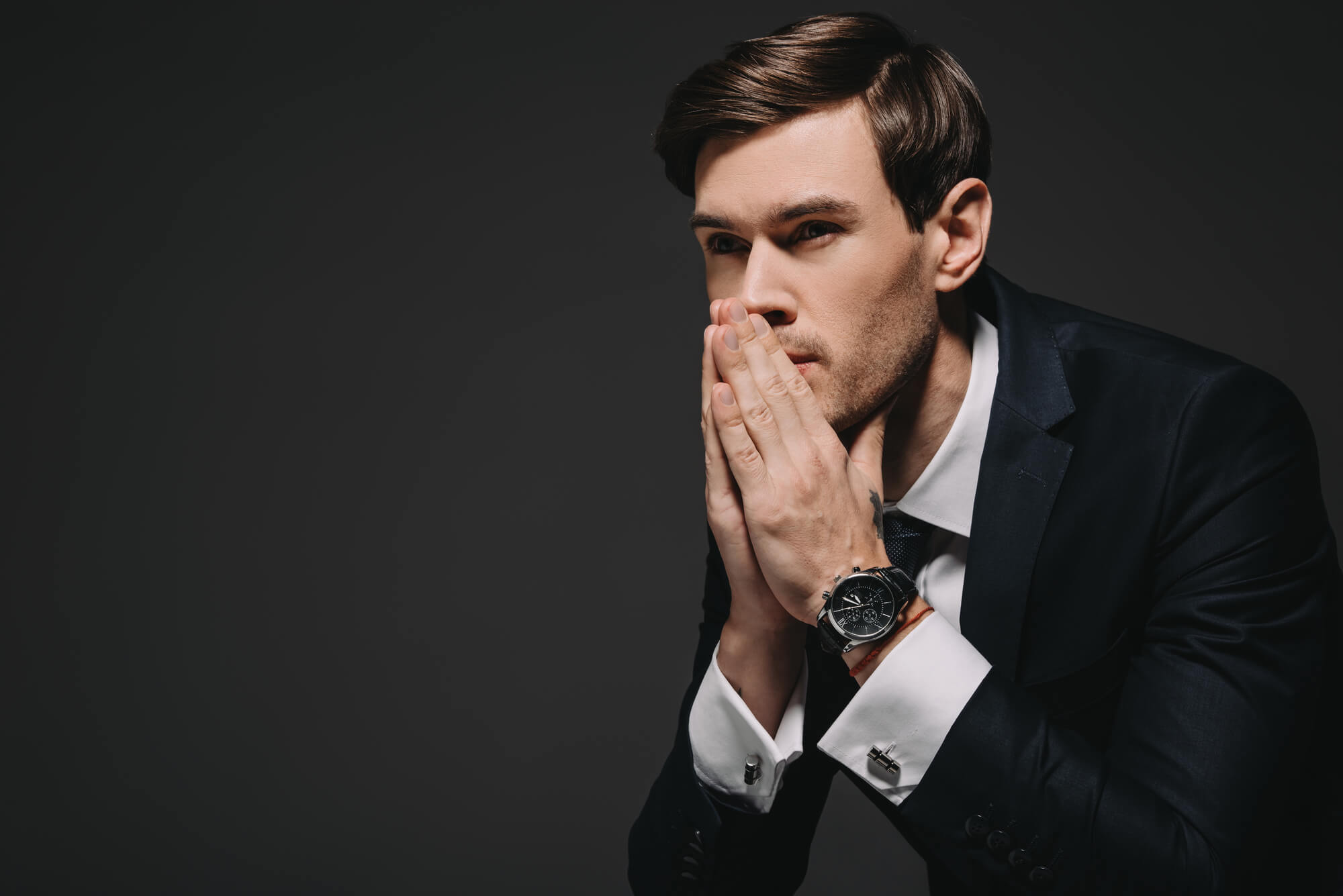 An attractive man in a suit holds his hands to his mouth as though deep in thought. Perhaps he could use the emotional benefits of TRT.