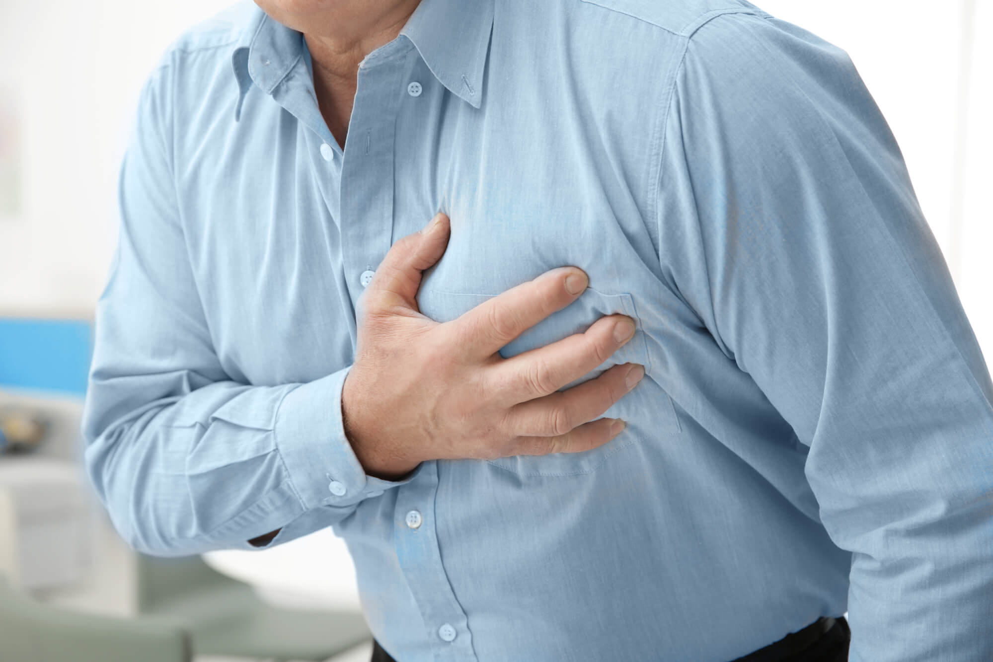 A man in a blue shirt clutches his chest. If he's had a history of heart trouble, he may be worried whether TRT is safe for him.