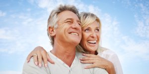 A middle-aged couple smile and embrace against a blue sky. Their lives have improved due to the TRT benefits to sexual performance.