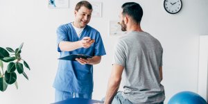 A doctor in scrubs talks to a male patient who sits on the exam table. Men's estrogen levels are something that should be discussed with your medical provider.
