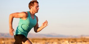 White male in a blu tank top is running across a desert landscape. Many people ask, "Does running boost testosterone?"