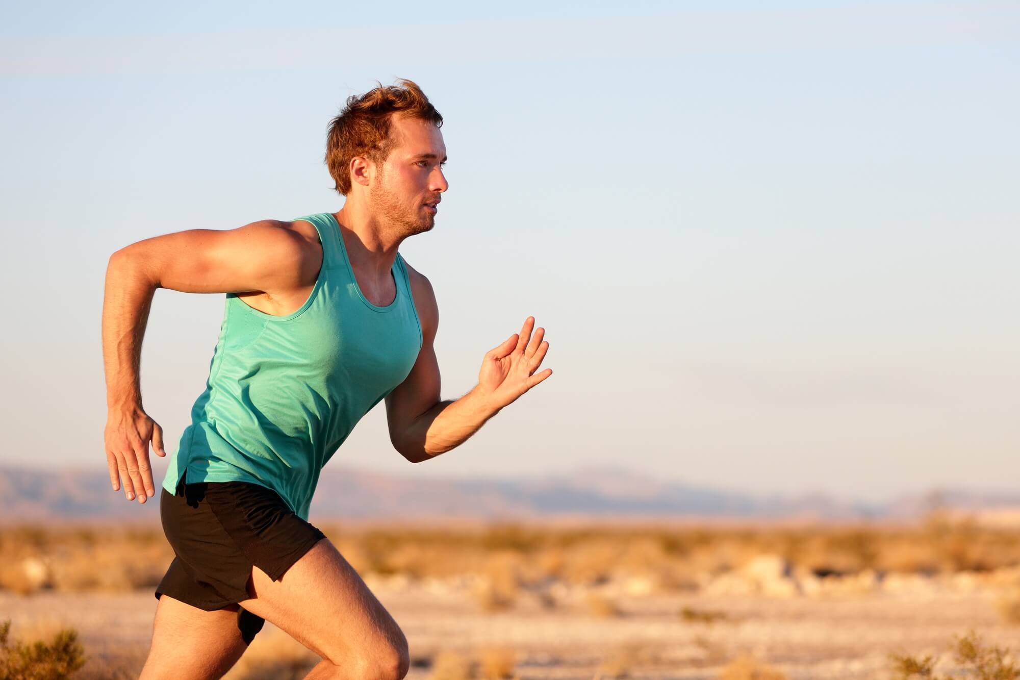 White male in a blue tank top is running across a desert landscape. Many people ask, "Does running boost testosterone?"