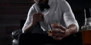 Man in a white shirt and bow tie looks at the glass in his hand, wondering if drinking alcohol is causing his Low T symptoms.