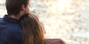 A woman sits with her head on a man's shoulder as they look at the water. There is a decline in male fertility that may complicate their relationship in the future.