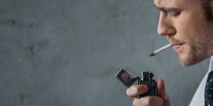 A man in a shirt and tie lights a cigarette. But, does smoking decrease testosterone? Yes, and no.
